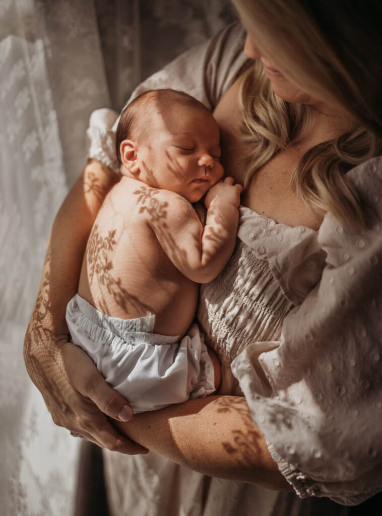 mother holding newborn baby during in-home newborn photos photoshoot