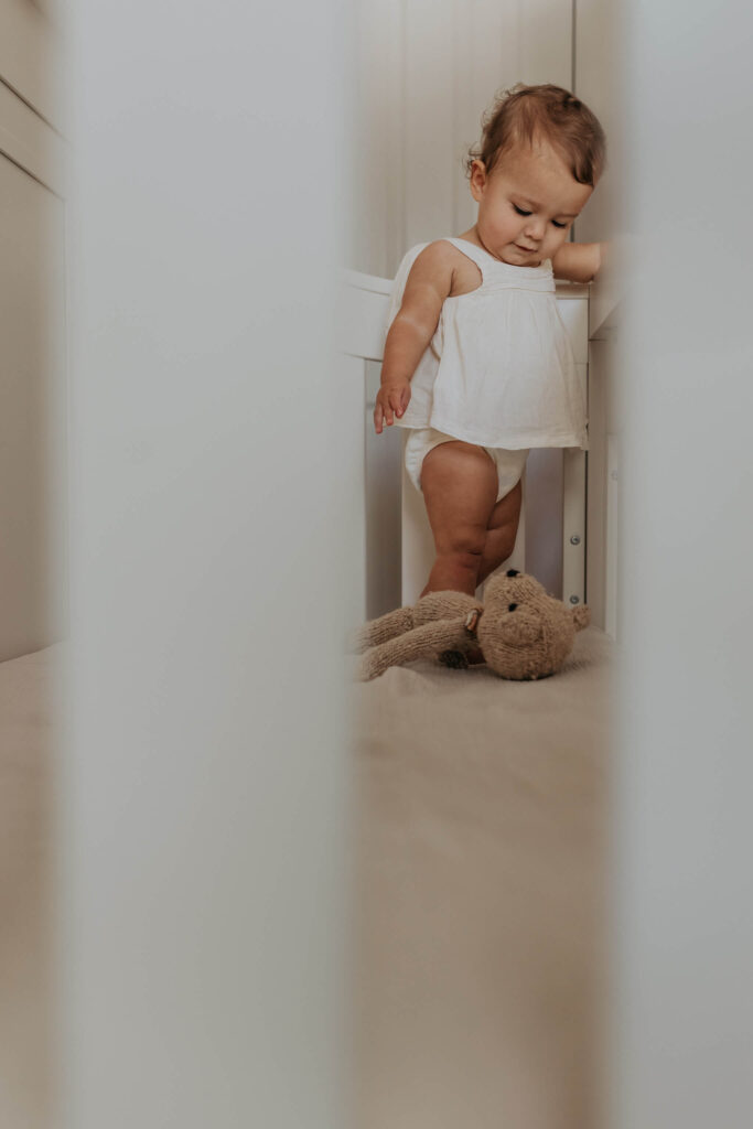 one year old girl playing with a bear in a crib