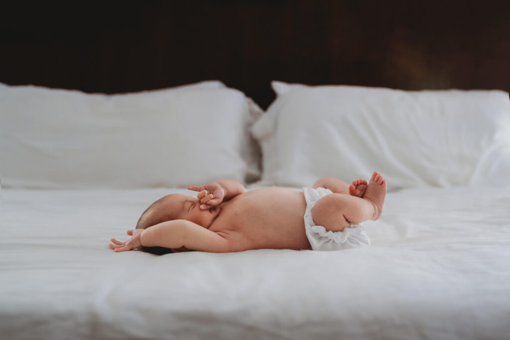 newborn baby stretching on bed during her newborn photos