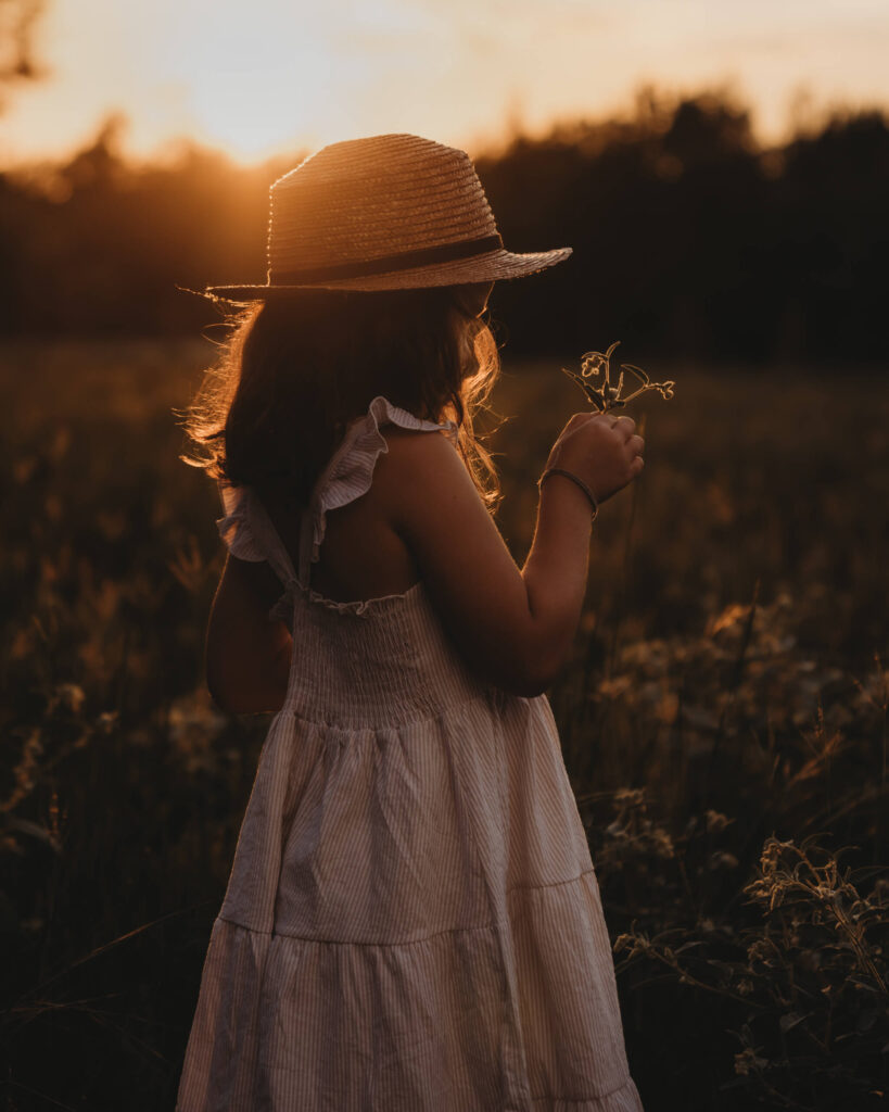 little girl holding flower with hat on during sunset. stressfree golden hour photoshoot