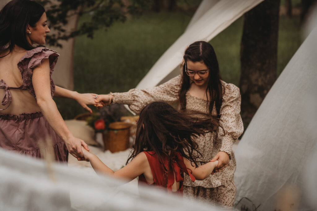 two kids and a mom holding hands in a circle dancing to music during their mommy and me photoshoot