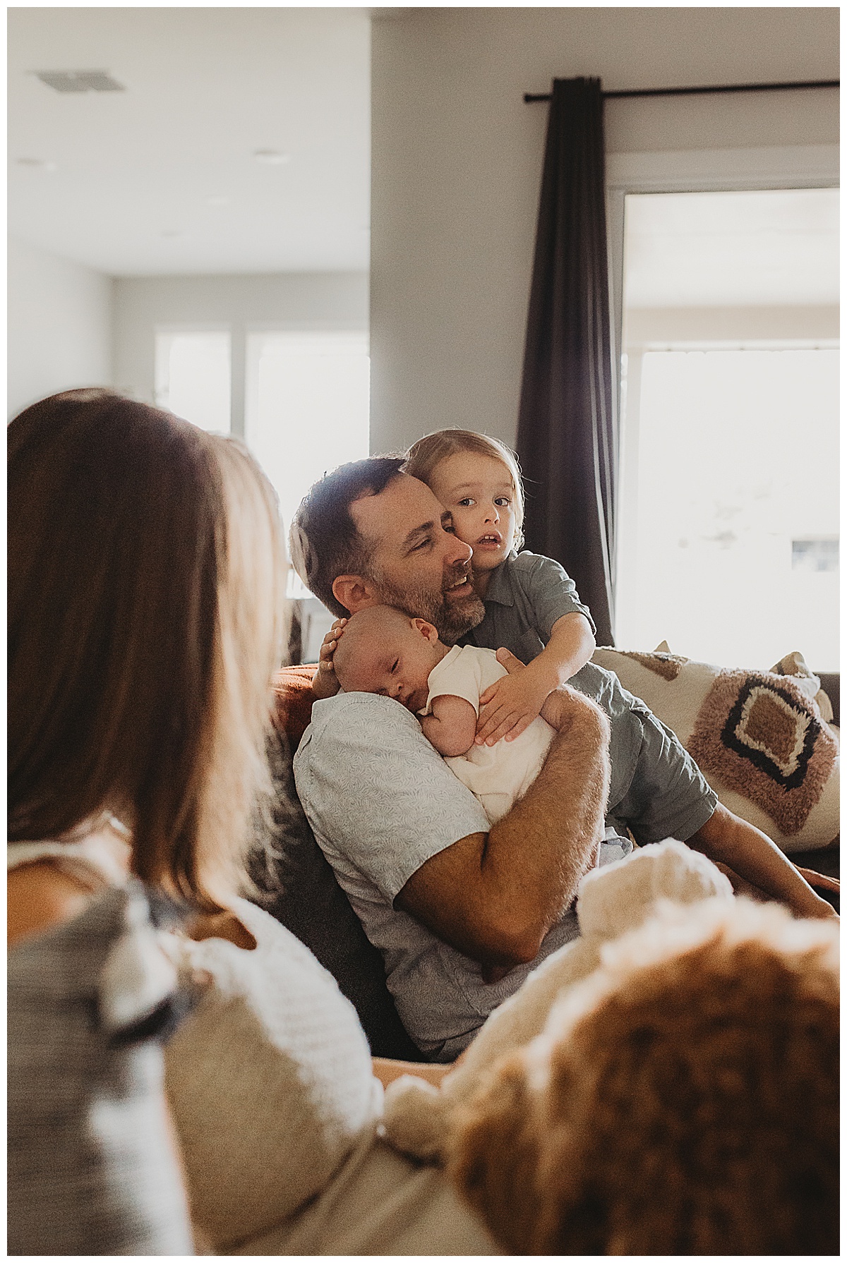 Family sit together on a couch showing Why You Should Choose An In-Home Newborn Session 