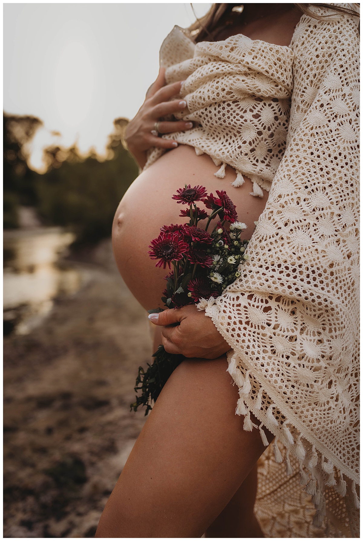 Mother holds flowers to her baby bump by Maria Grace Photos