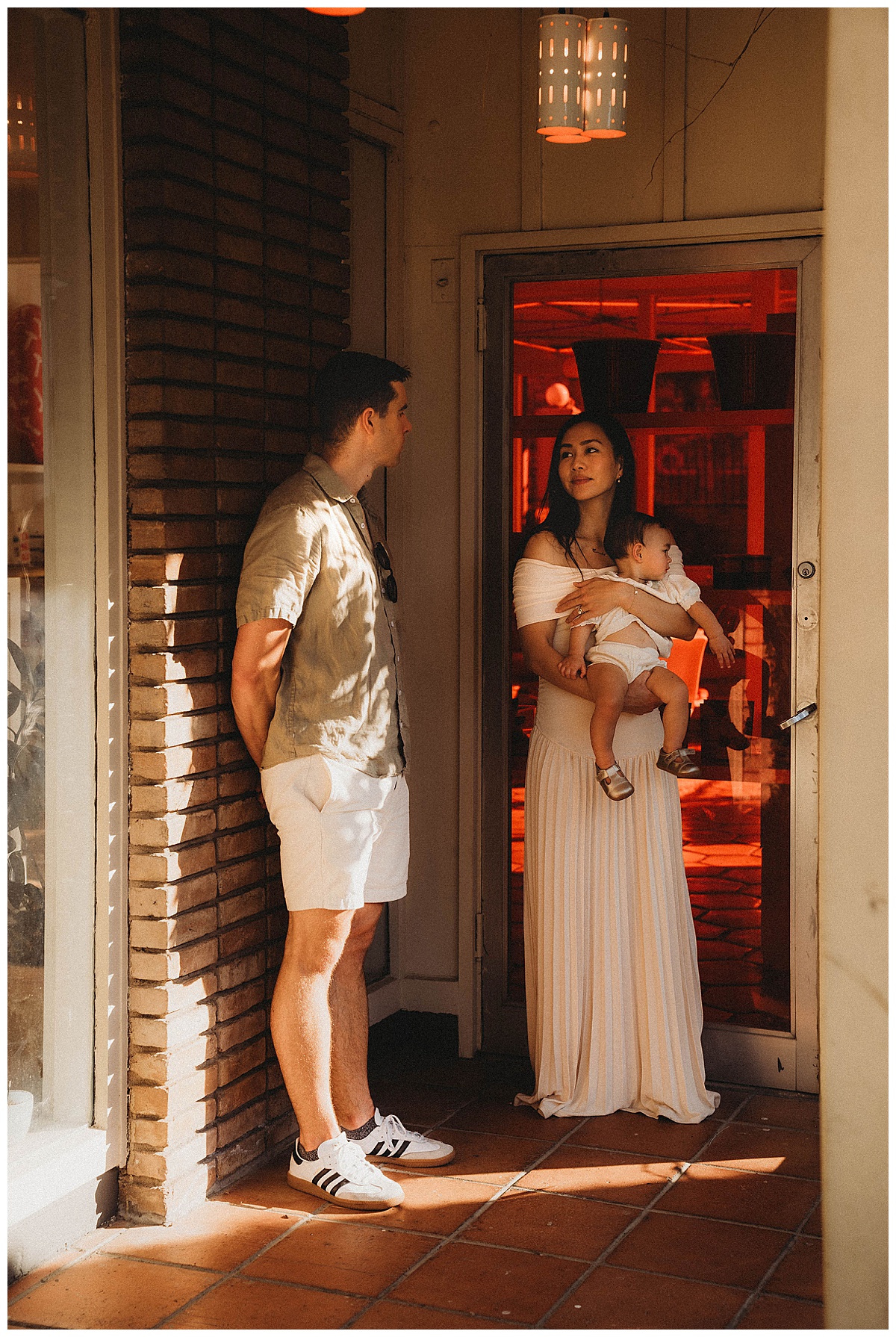 Parents stand against a wall holding their baby for Maria Grace Photos