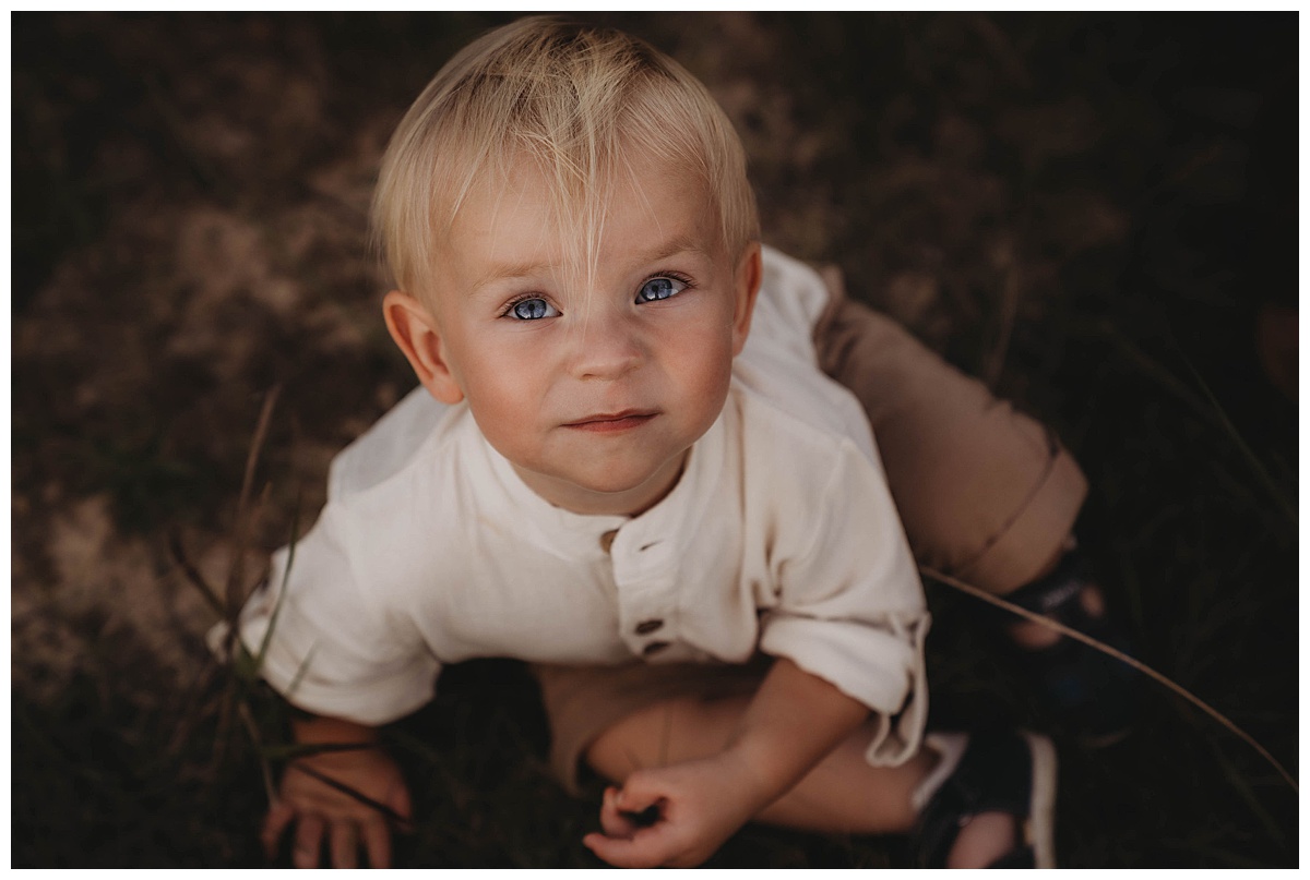 Young boy sits on the ground looking up following my suggestion of Golden Hour for Family Photos